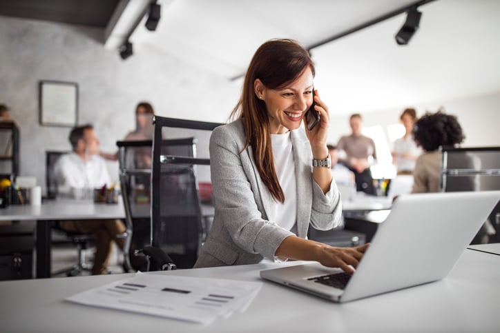 Woman working in office talking on the phone and using laptop