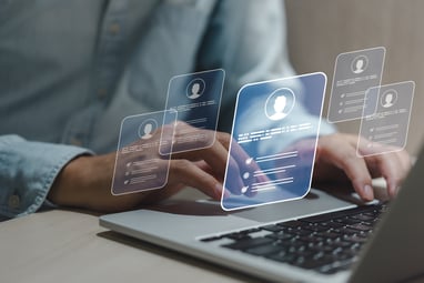 person typing on a computer with virtual applicants hovering over the computer holographically. 