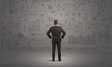A successful confident businessman thinking about decisions, standing in front of wall full with graph pie charts and calculations concept