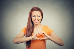 Closeup portrait smiling cheerful happy young woman making heart sign with hands isolated grey wall background. Positive human emotion expression feeling life perception attitude body language