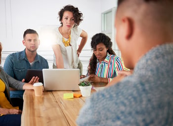 Multi ethnic group of succesful creative business people using a laptop during candid meeting-1