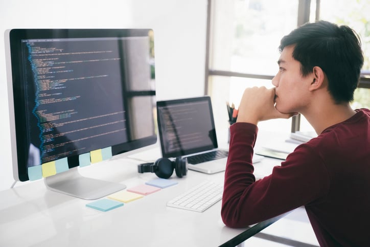 A software tester sits at a desk, reviewing a codebase displayed on their monitor