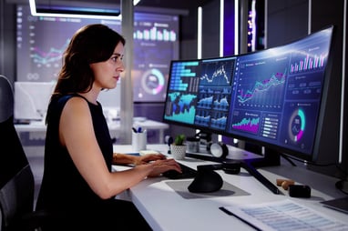person sitting in an office chair looking at dual monitors that are showing a variety of dashboards