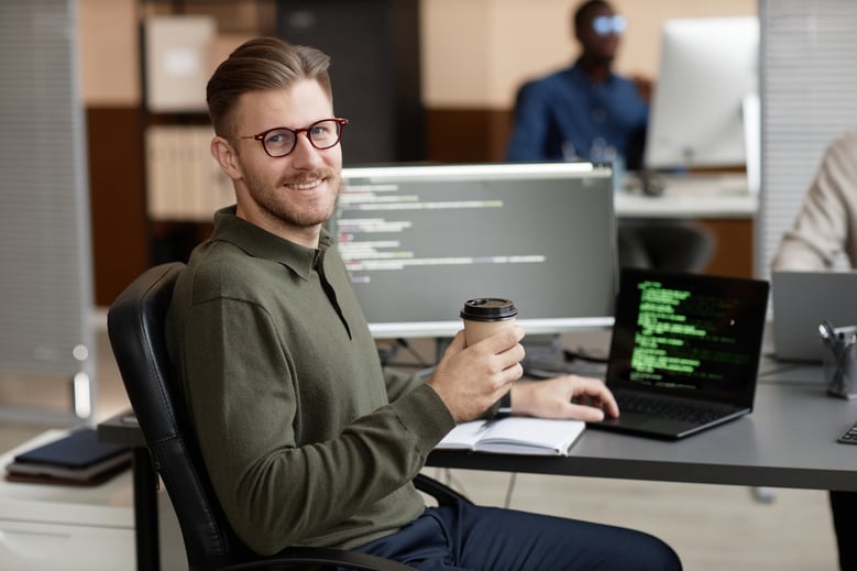 software developer holding a coffee while sitting in front of a computer desk