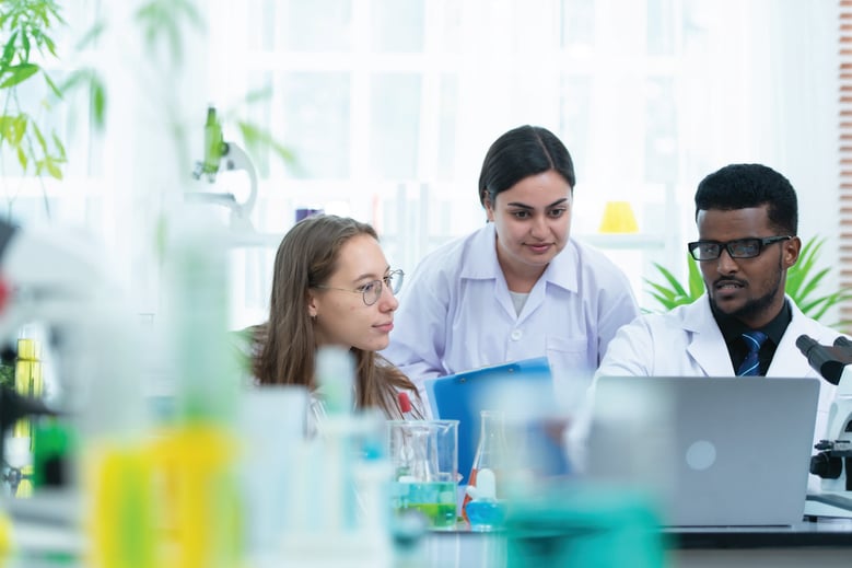 Three medical affairs professionals in lab coats, all focused on a computer screen.