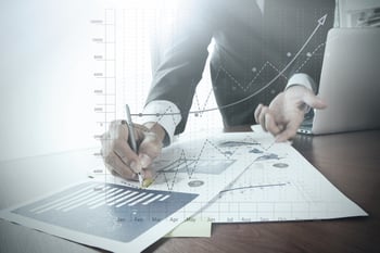 close up of businessman hand working on laptop computer with business graph information diagram on wooden desk as concept