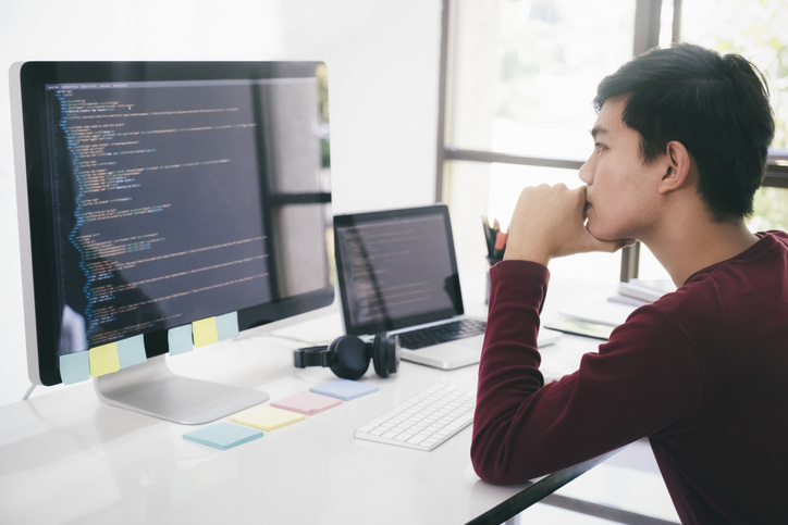 A software tester sits at a desk, reviewing a codebase displayed on their monitor