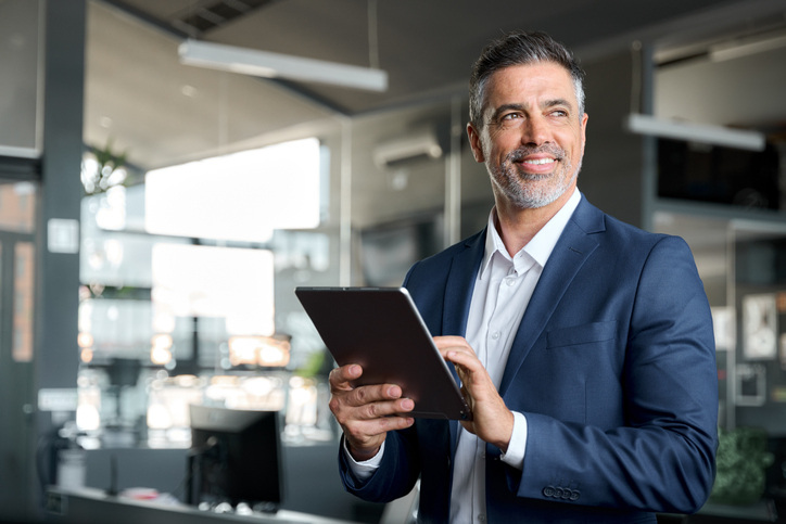 A cybersecurity executive in a navy suit, holding a tablet and gazing thoughtfully into the distance