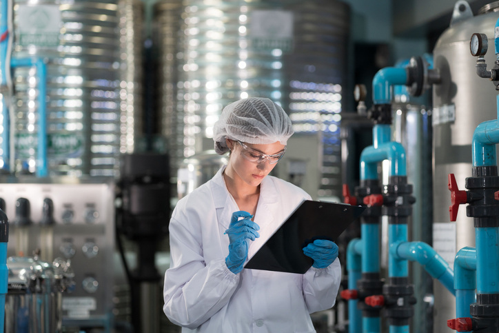 Female worker wearing uniform, hairnet working and checking of water pump system, pipes station, Water pressure system, water tank at production line in industry factory